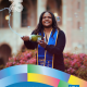 Cynamon Mantley ’18 smiles in front of UCLA’s Royce Hall while holding a bottle spraying celebratory bubbles. She wears a blue-and-gold graduation stole. Text identifies her fields of study as African American Studies and Italian and includes the CCCP 25 Years and UCLA logos.