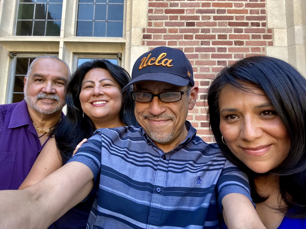 Carina Salazar and three other adults take a group selfie outside a brick UCLA building. One person wears a navy UCLA cap.