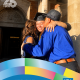 Andrea Arias, UCLA English Literature class of 2020, smiles while embracing two loved ones outside a campus building after graduation in a CCCP 25th anniversary–branded alumni graphic.