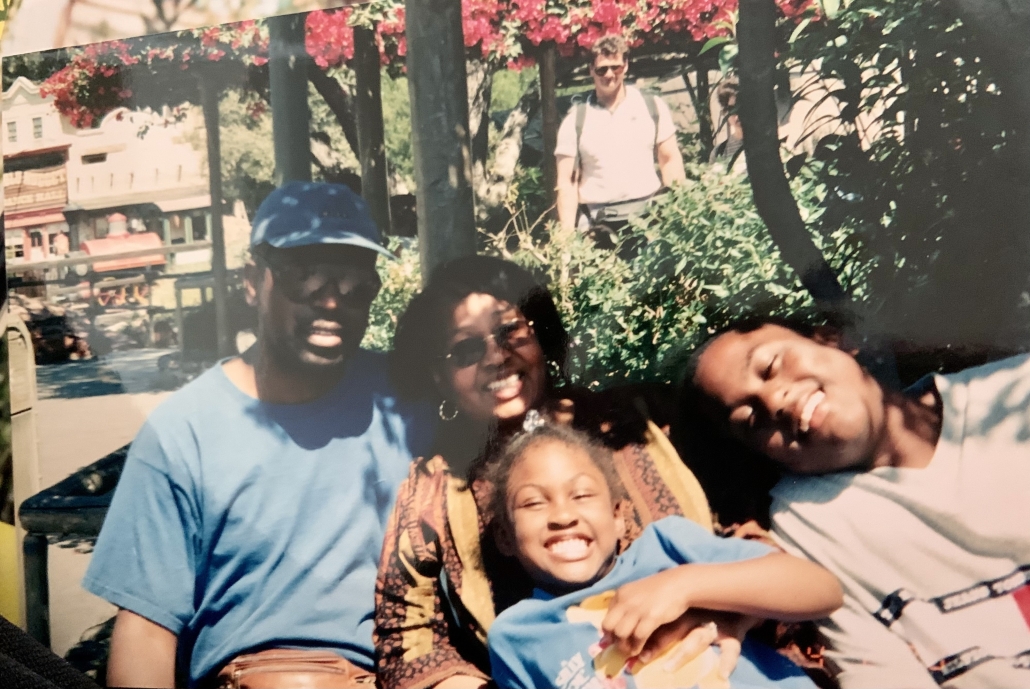 Jessica Hall smiles with three family members outdoors beneath flowering trees and greenery.