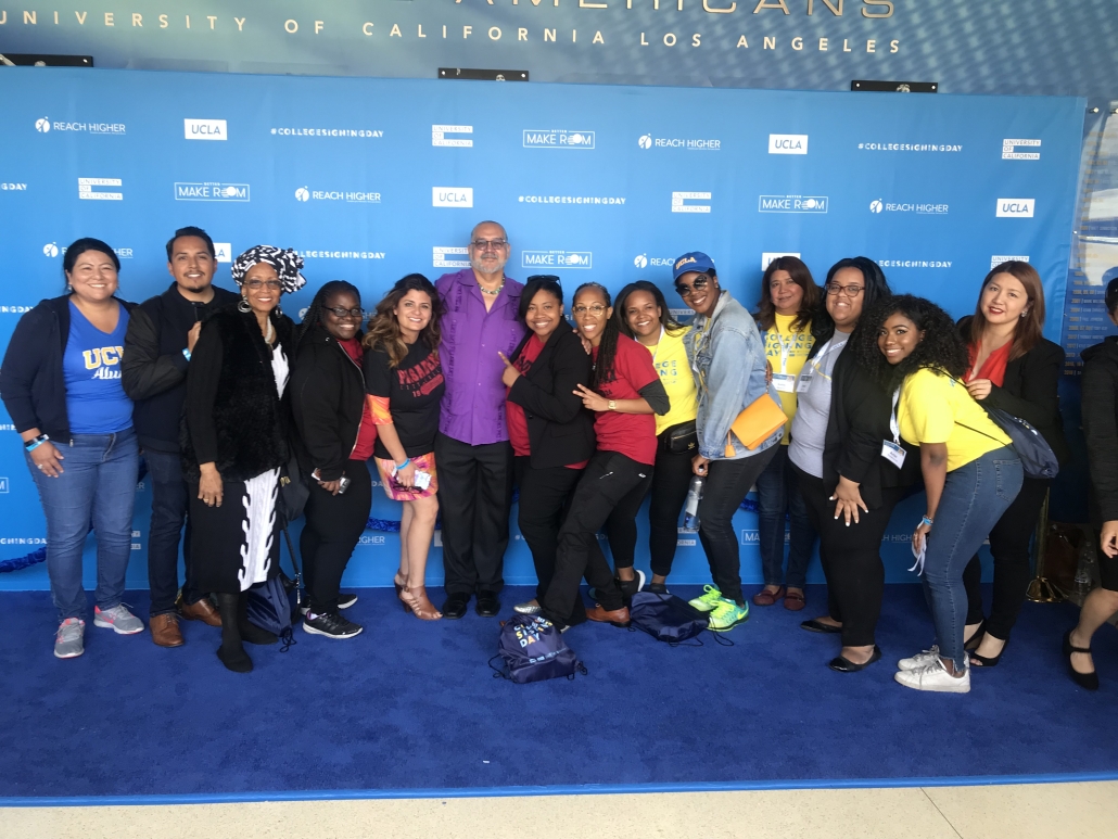 Aurelia poses with a large group of UCLA staff and supporters in front of a blue College Signing Day backdrop at UCLA.