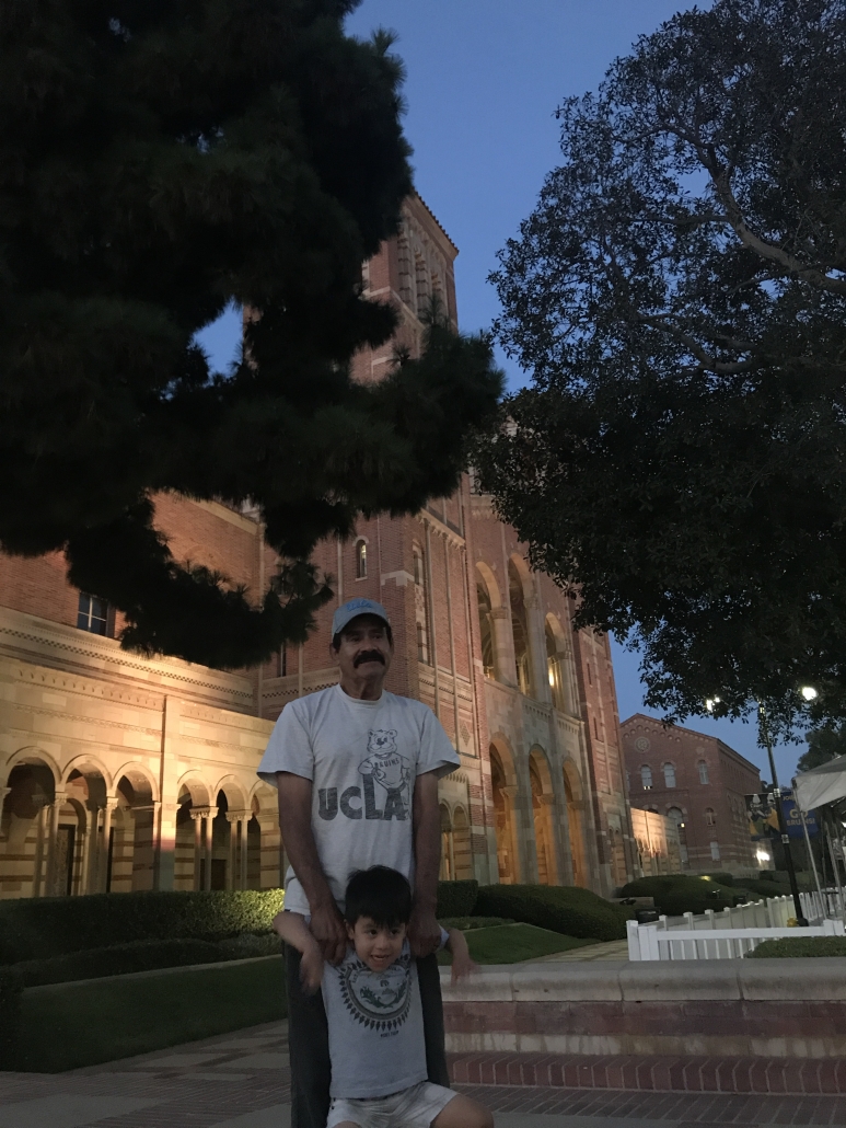 A man and young child pose together in front of Royce Hall on the UCLA campus at dusk.
