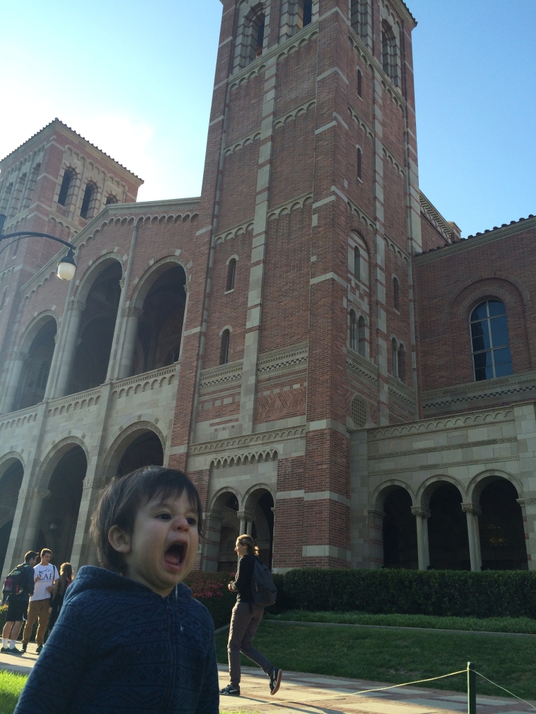 A young child opens his mouth excitedly while standing in front of Royce Hall on a sunny day.