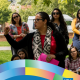CCCP 25th anniversary profile graphic featuring Christine Vega speaking outdoors to a group of students while holding a bright pink folder. She wears glasses, a red top, black cardigan, and a black-and-white patterned scarf. The white CCCP 25 Years logo appears at the top left, colorful curved ribbon graphics frame the bottom, and the UCLA logo appears at the lower right. Text reads: “Christine Vega ’07, Ph.D. ’19, Women & Gender Studies and Chicana/o Studies, Education and Comparative Race and Ethnic Studies.”