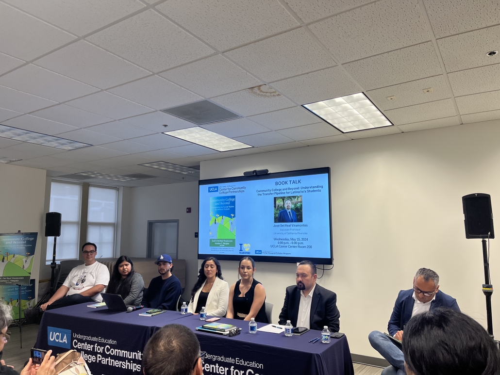 A panel of seven speakers sits at a table during a UCLA Center for Community College Partnerships book talk. A large screen behind them displays information for Community College and Beyond: Understanding the Transfer Pipeline for Latina/o/x Students by José Del Real Viramontes, including the event date, time, and location.
