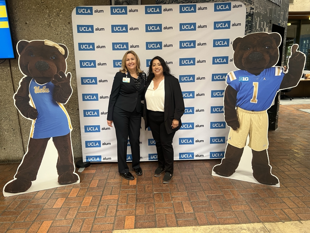 Aranzazu and another woman pose between life-size cutouts of UCLA mascots Joe and Josephine Bruin in front of a UCLA Alumni backdrop.