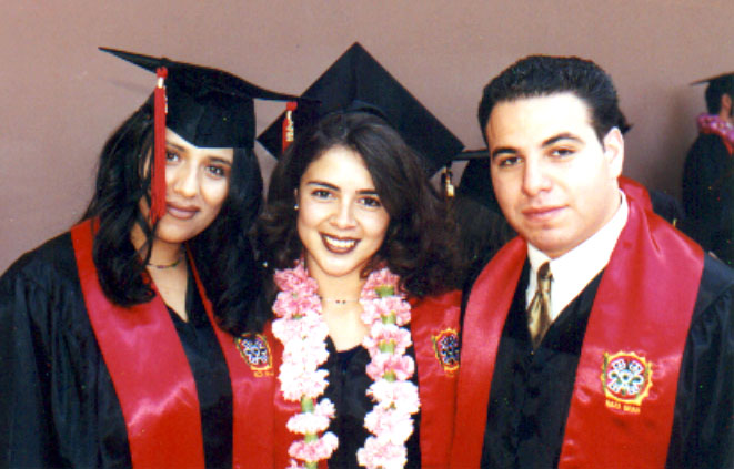 Carina Salazar poses with two fellow UCLA graduates in black caps and gowns with red graduation stoles. The graduate in the center also wears a pink floral lei.