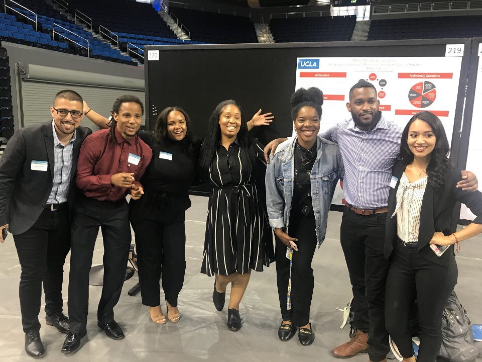 Cynamon Mantley poses with six colleagues in front of a research poster during an indoor UCLA event.