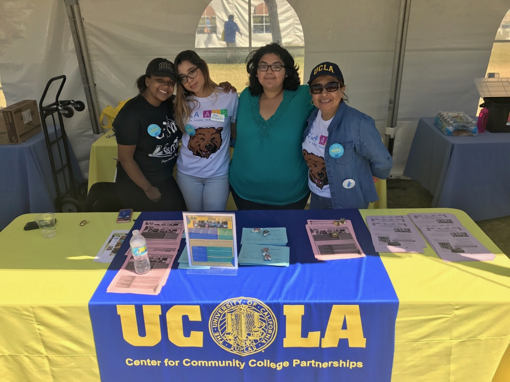 Cynamon Mantley and three colleagues stand behind a UCLA Center for Community College Partnerships information table inside an event tent.